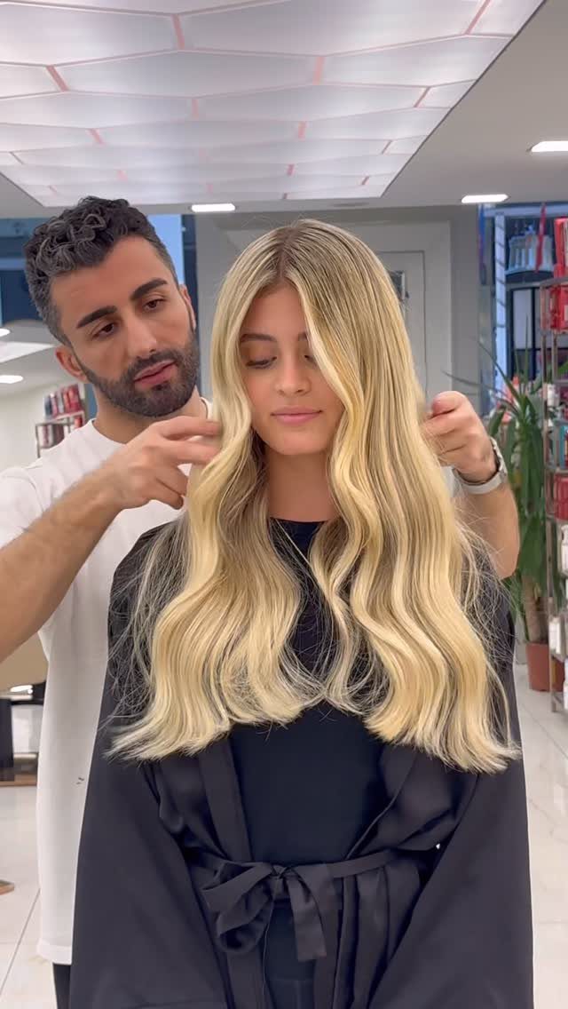 Long beige-gold blonde waves with darker roots in a salon
