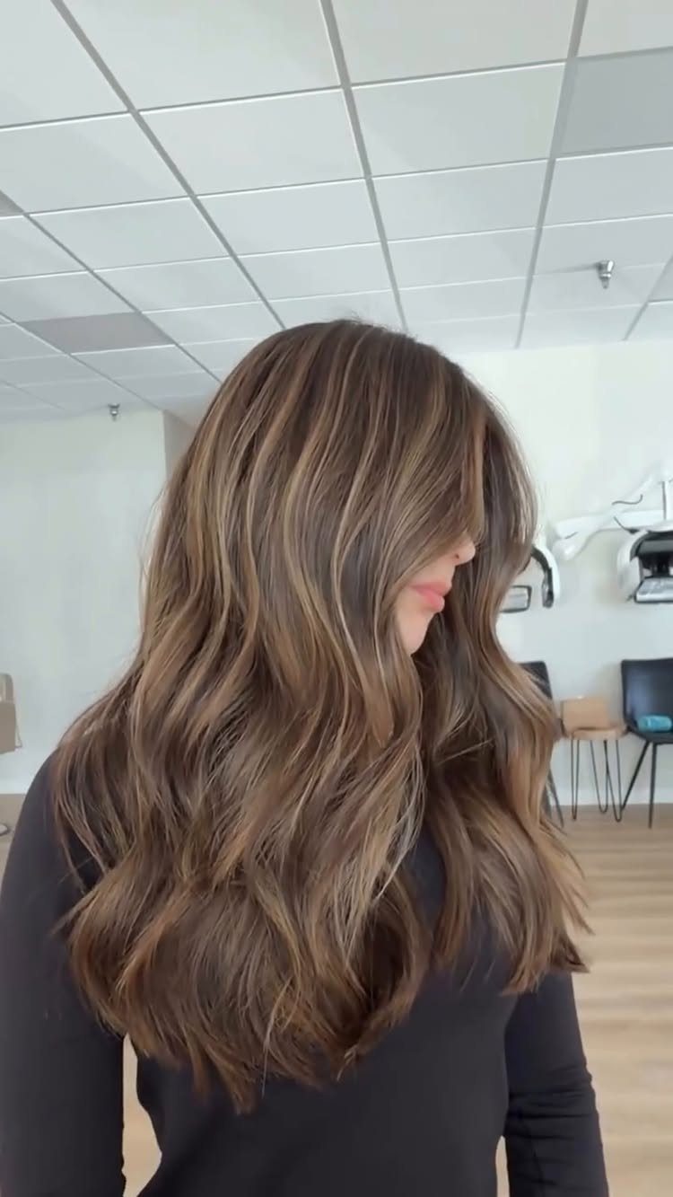 Long wavy brown hair with soft caramel balayage highlights in a salon
