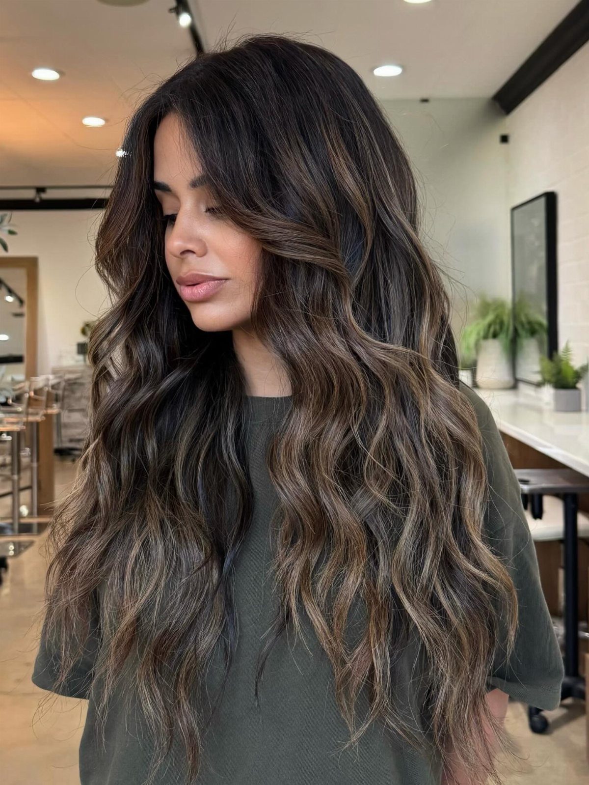 Woman with long brunette waves showing seamless caramel highlights in a salon