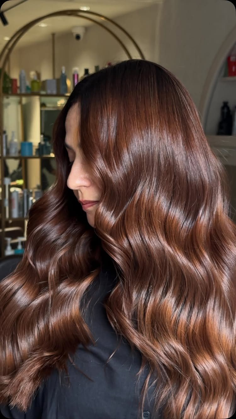 Woman showing long glossy cinnamon auburn waves in a salon
