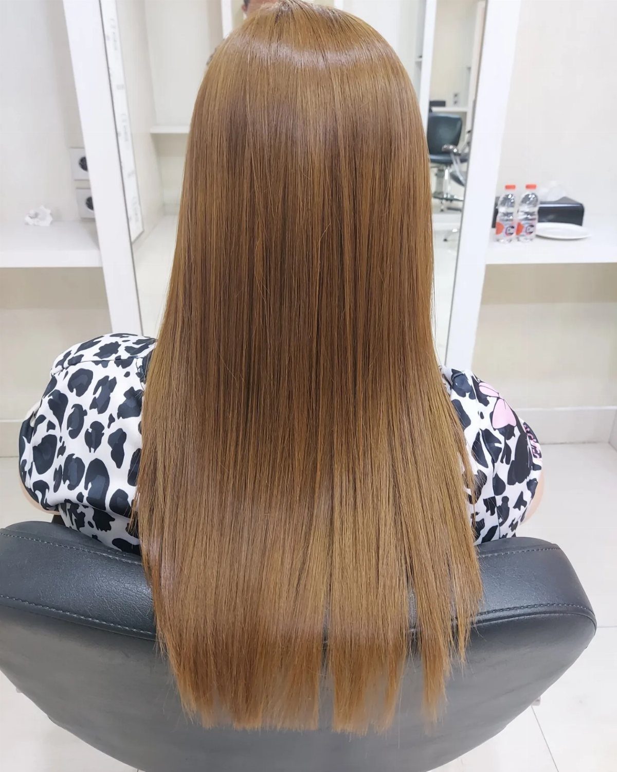Long, glossy golden-brown hair falls straight down a salon client's back