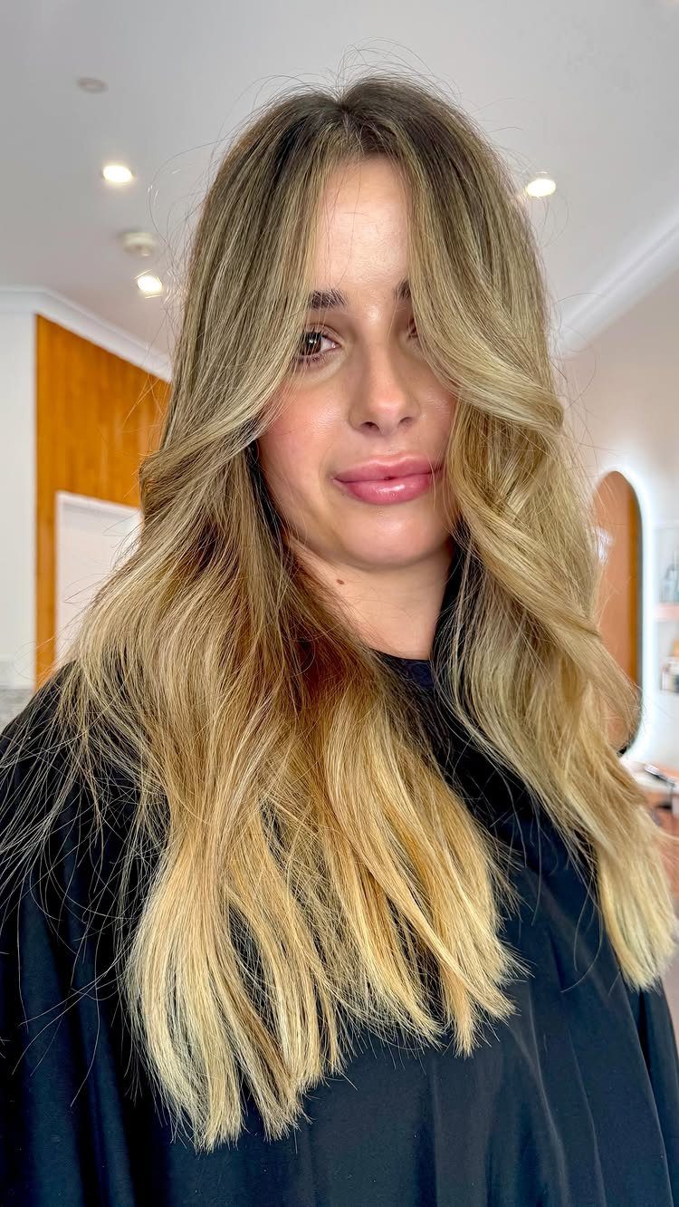 Woman with long, layered honey-blonde hair and darker roots