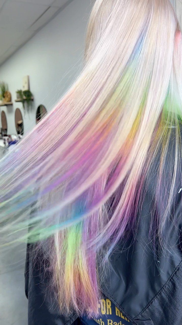 Pastel rainbow streaks run through long platinum-blonde hair in a salon