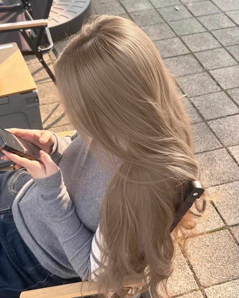 Long beige-blonde hair falls in smooth waves over a grey top