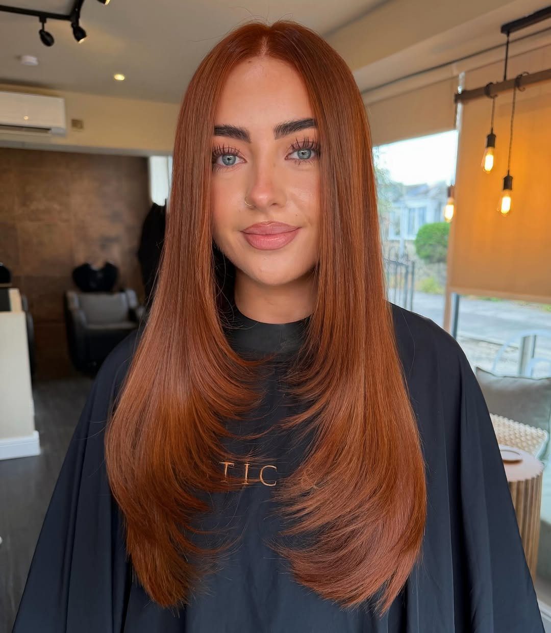 Woman with long, glossy copper-red hair posing in a salon chair