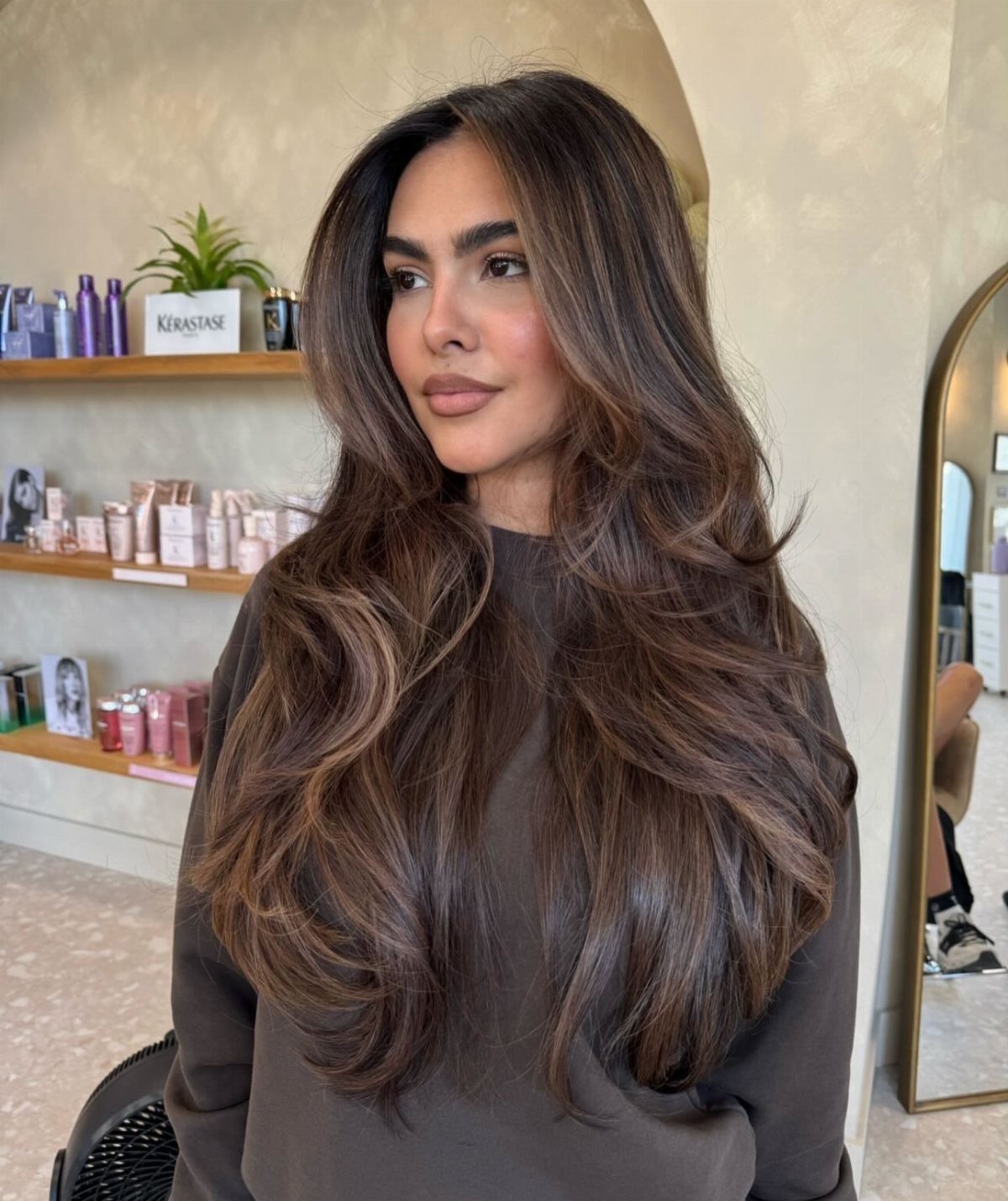 Woman with long, voluminous brunette hair and warm brown highlights