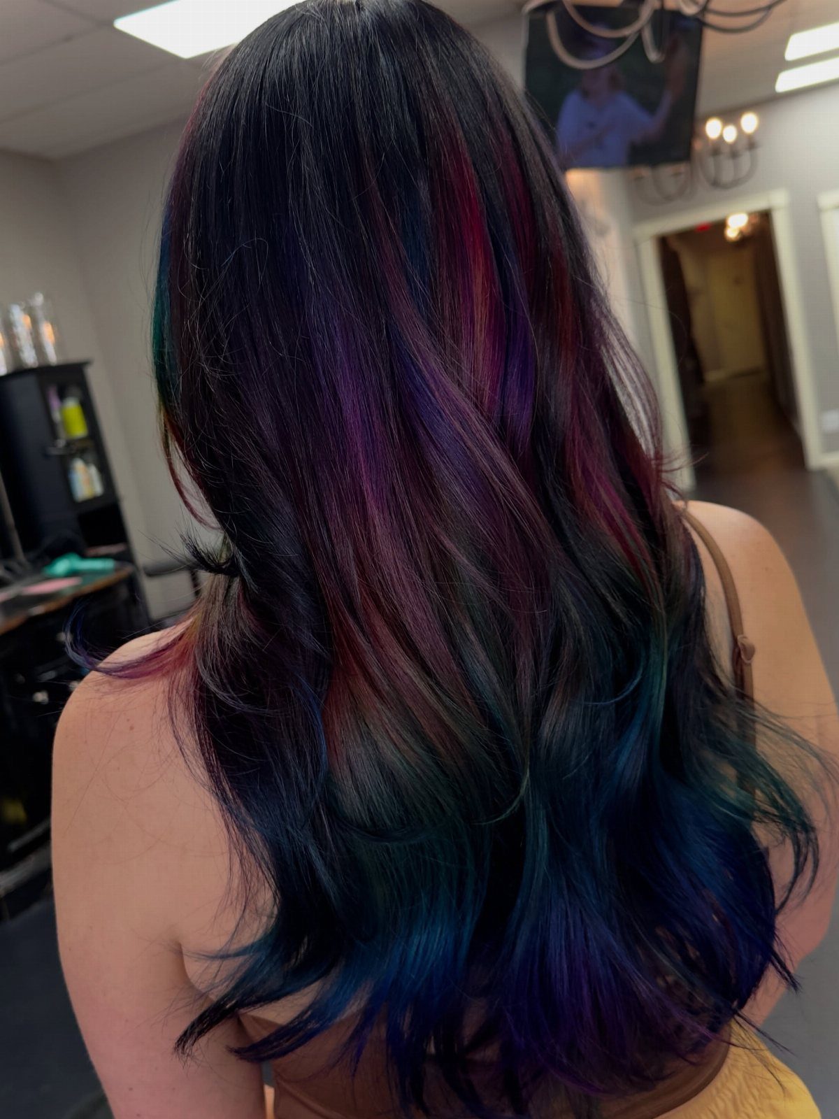 Long dark wavy hair shows blue and purple highlights in a salon