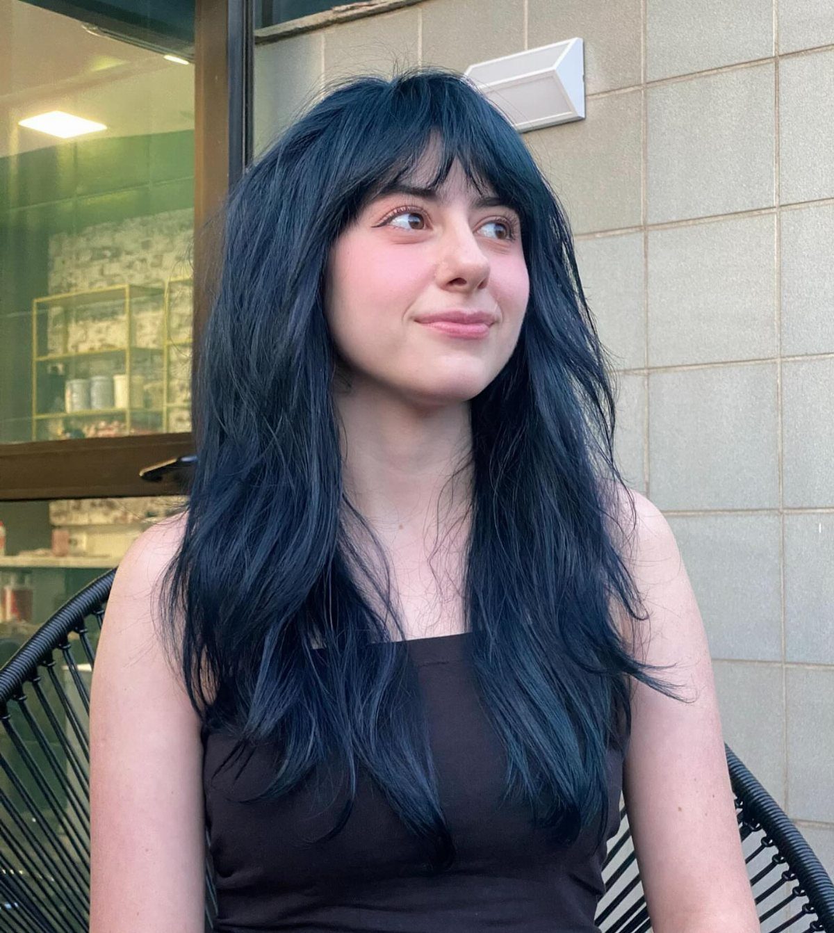 Woman with long wavy dark blue hair and bangs seated outside