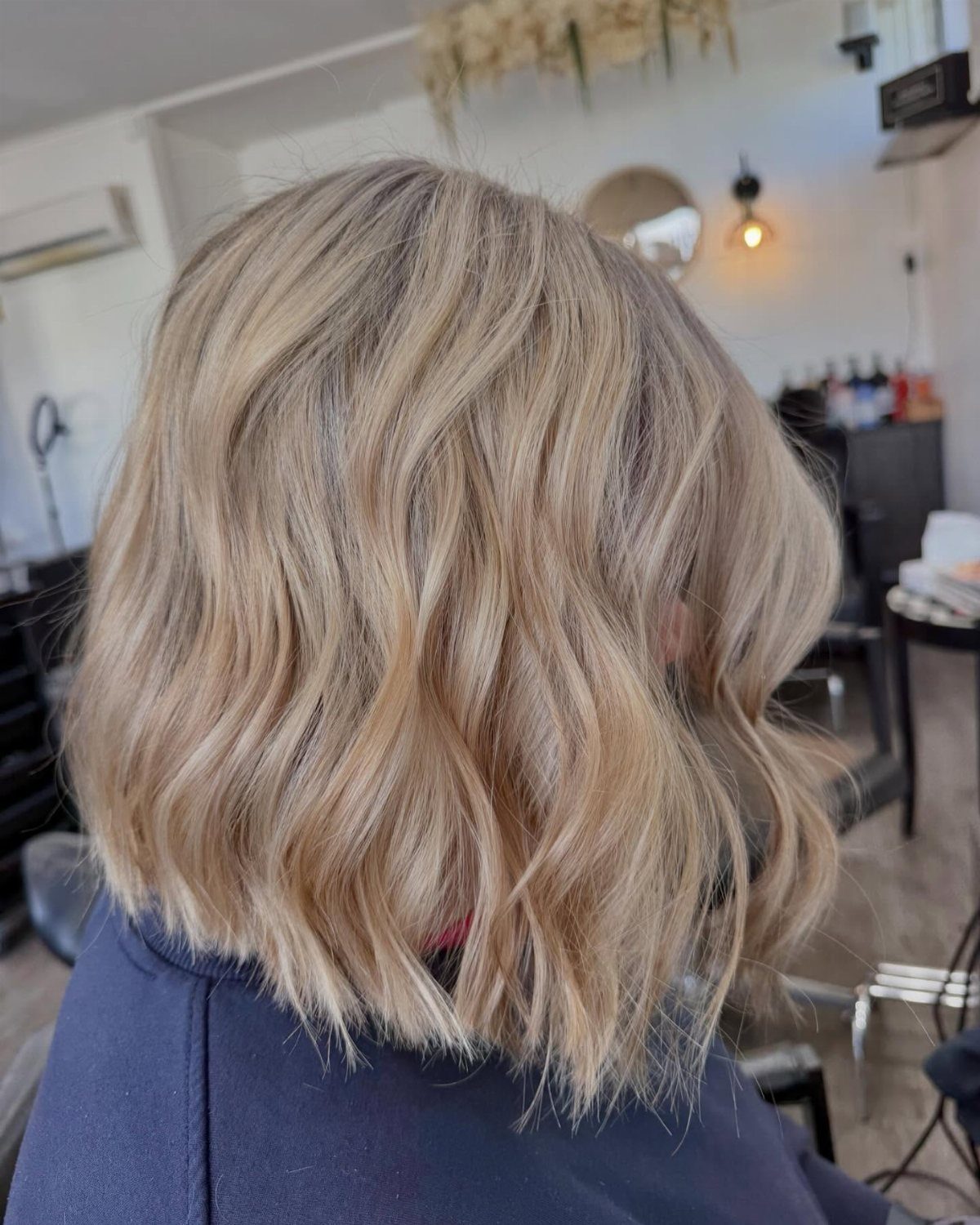 Wavy blonde and grey shoulder-length hair with darker roots in a salon