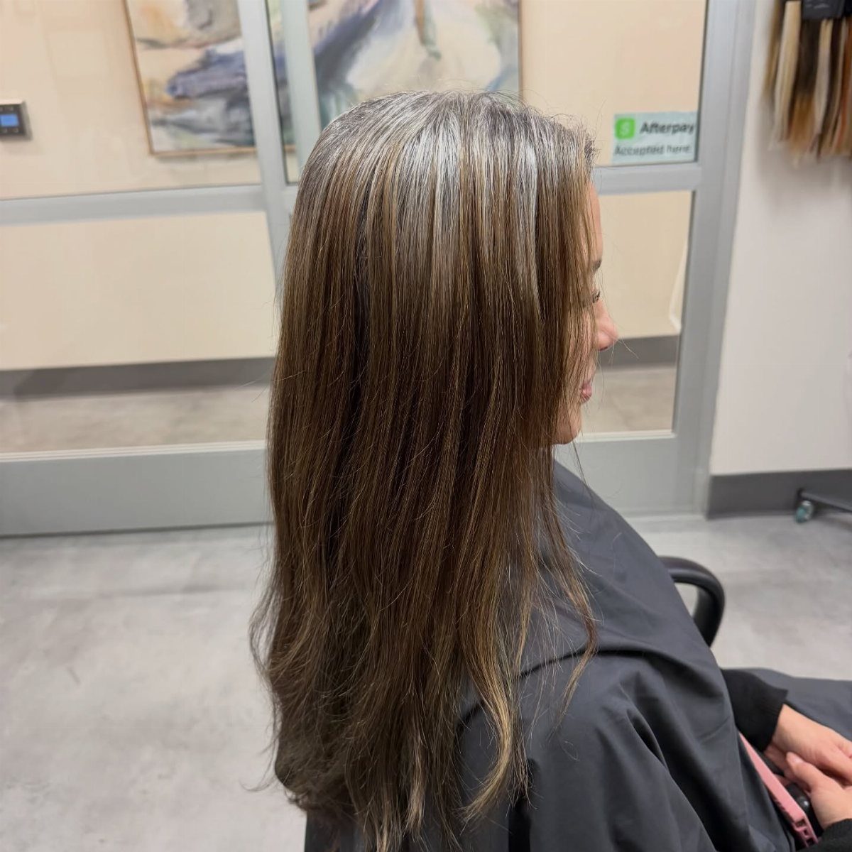 Long brown hair with blended silver-grey strands shown from the side in a salon