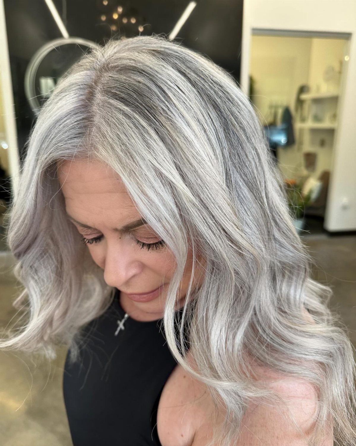 Woman showing long, wavy blended grey hair with darker roots in a salon