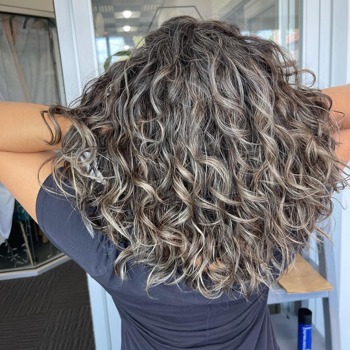 Curly dark hair with silver-gray streaks falls to the shoulders in a salon