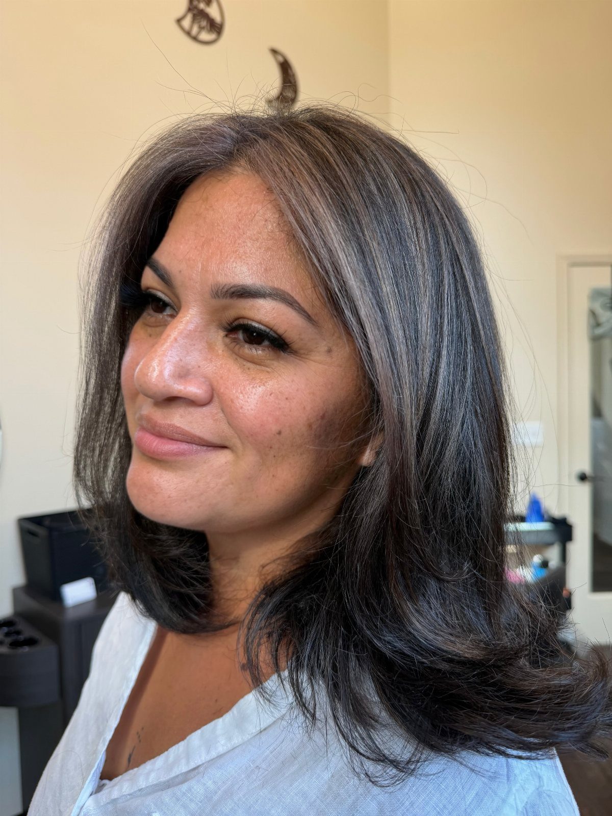 Woman with shoulder-length dark hair showing fine silver-gray streaks and layered ends.