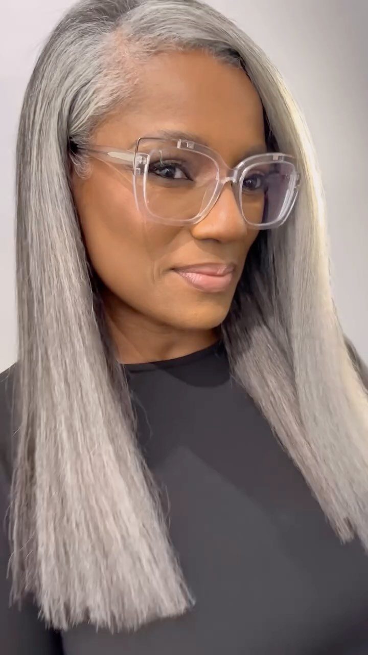 Woman with long, straight silver-gray hair and darker roots wearing clear glasses