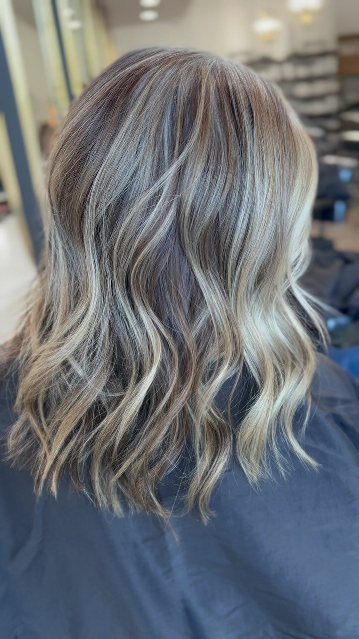 Wavy brown hair with blended silver-gray highlights cascading over a dark salon cape