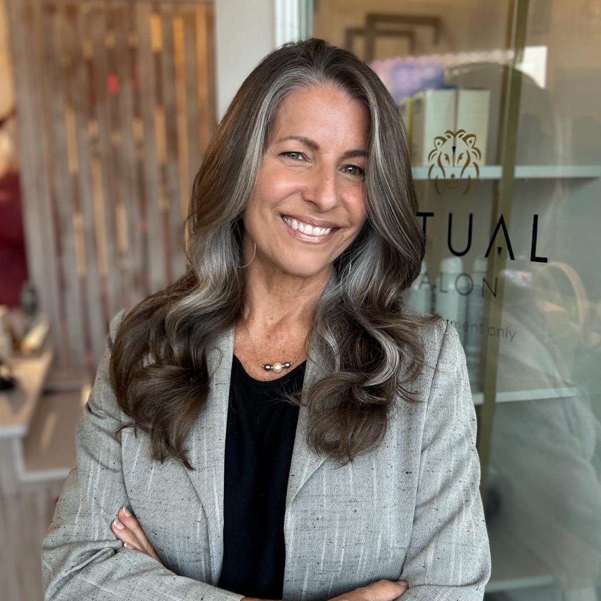 Woman with wavy dark hair and silver-gray face-framing streaks outside a salon