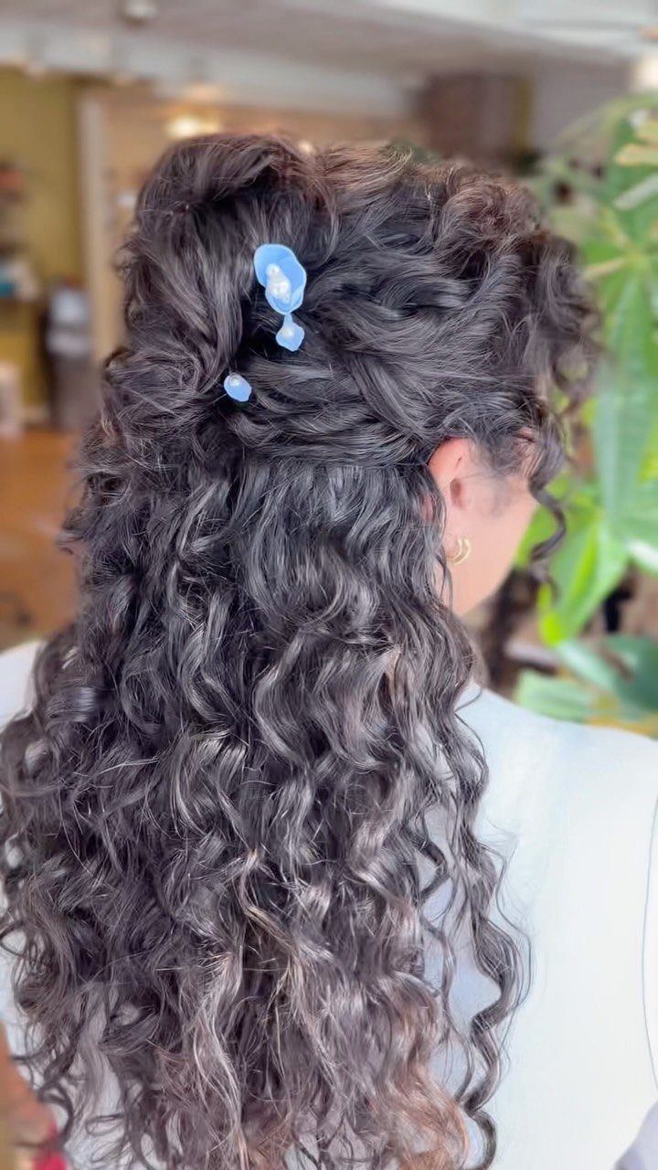 Long dark curls pinned back with a light blue clip cascade over the shoulders