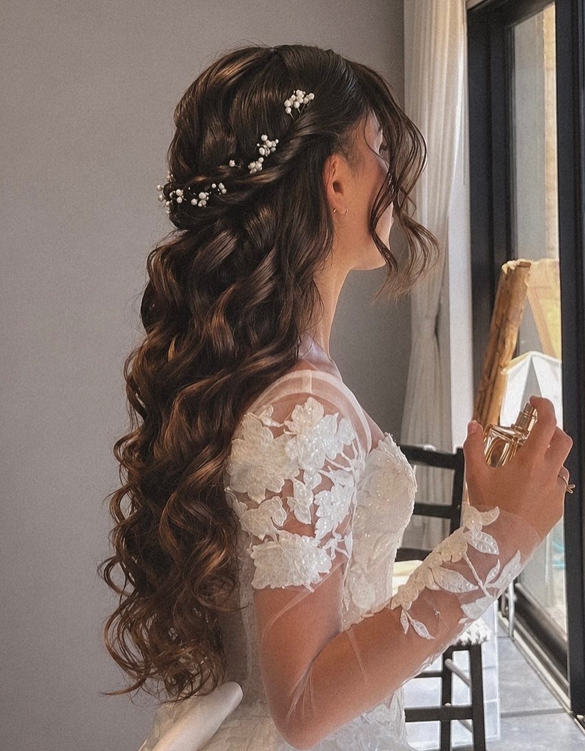 Bride with long pinned-back waves and pearl hair ornaments beside a window
