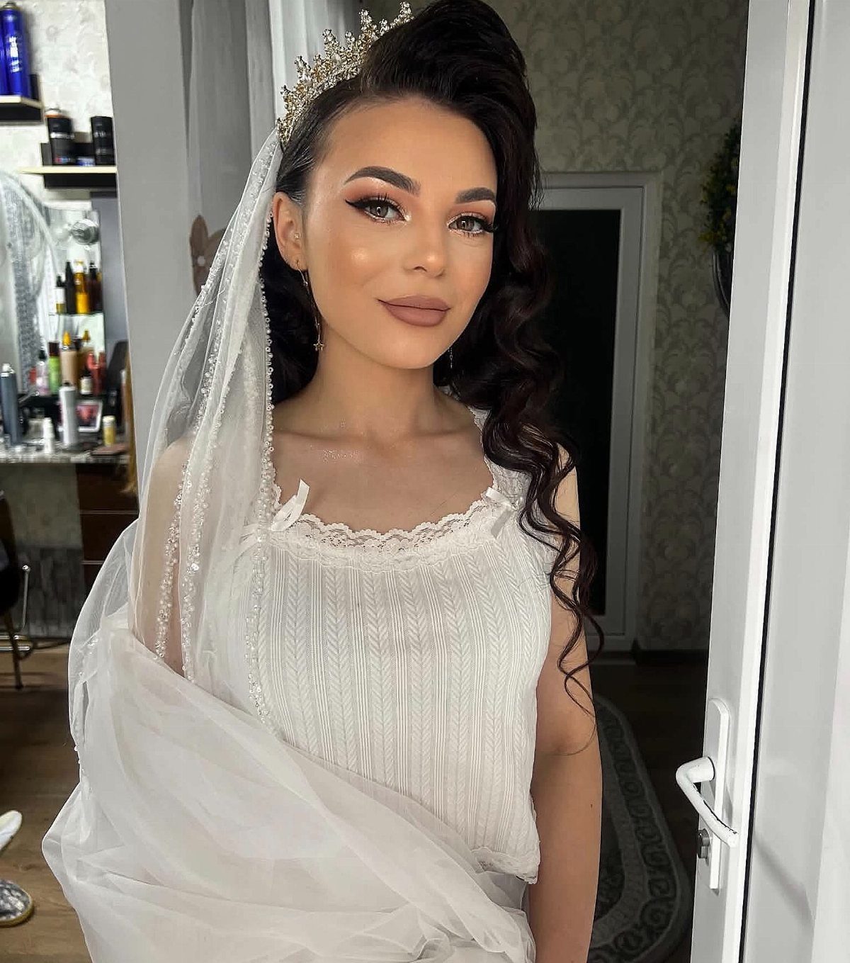Bride wears a sparkling tiara and veil with dark side-swept curls