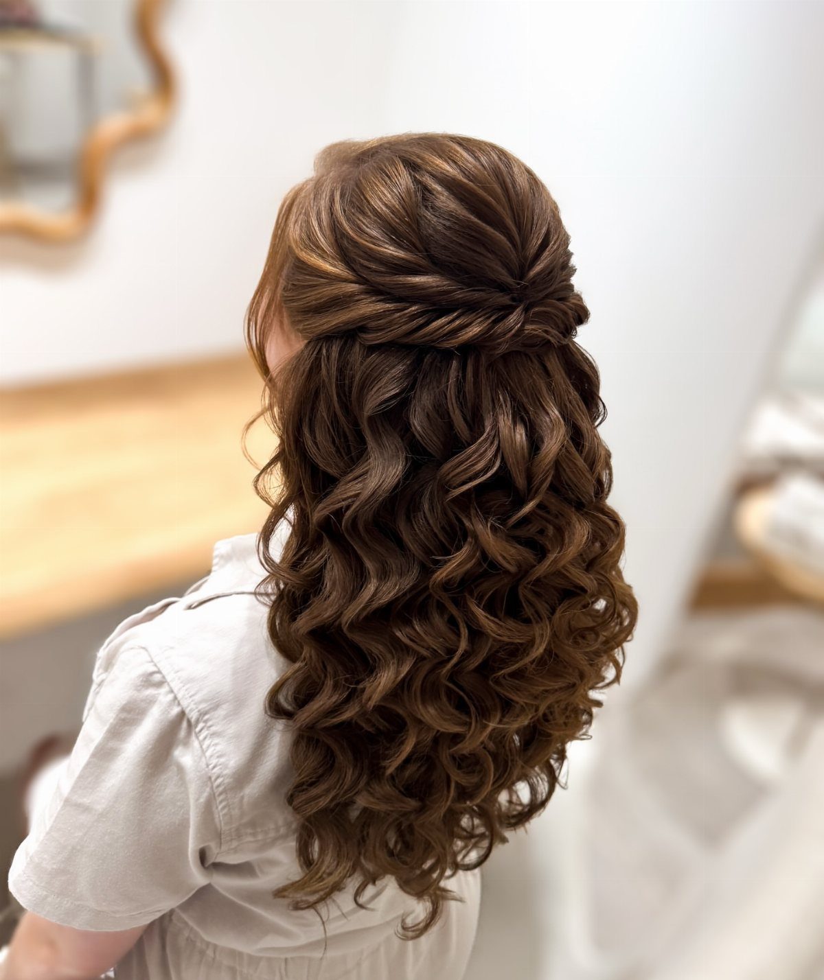 Half-up brown hairstyle with twisted sections pinned above long cascading curls
