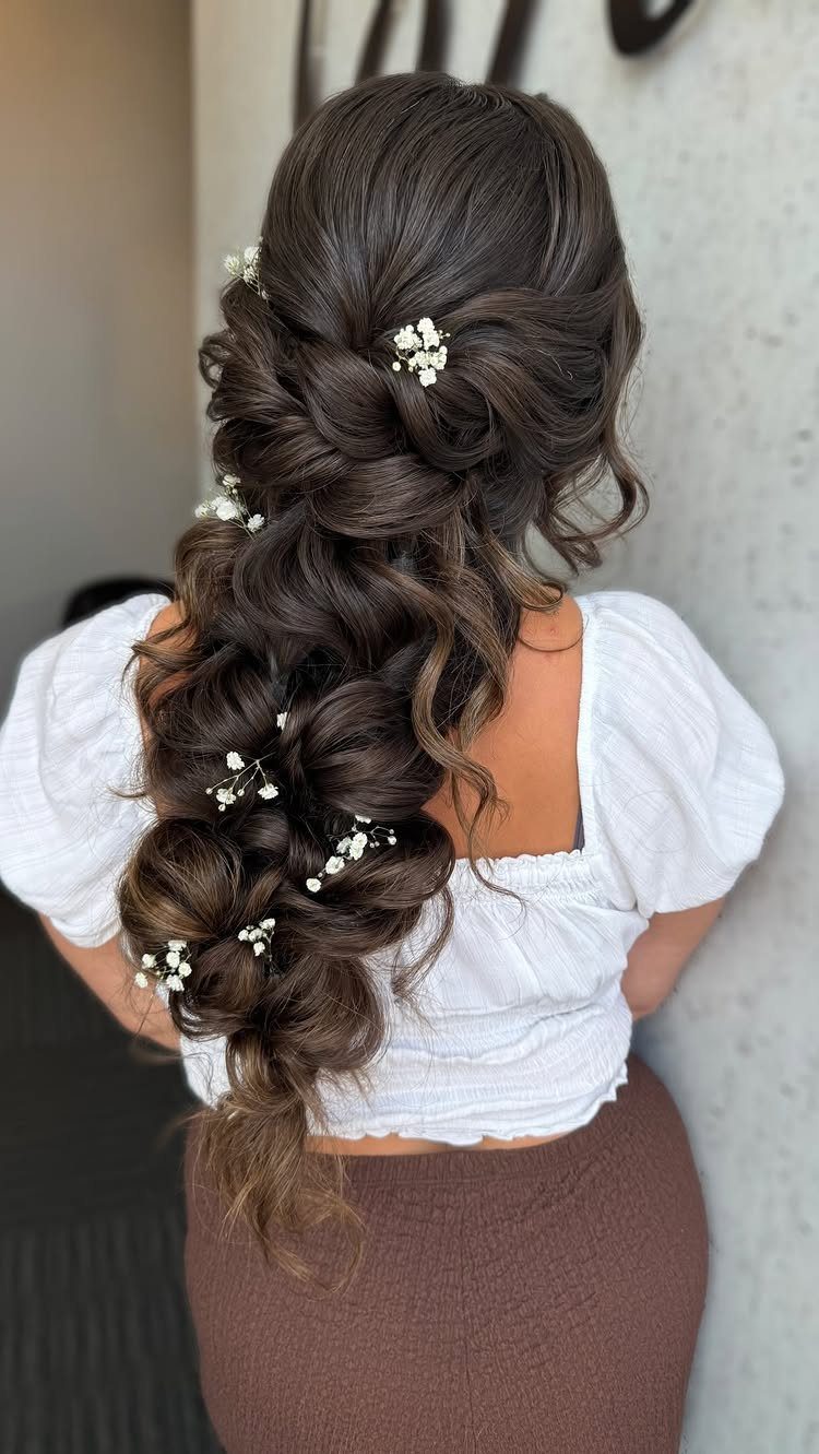 Long dark hair pulled back into voluminous layers and cascading curls with white flowers
