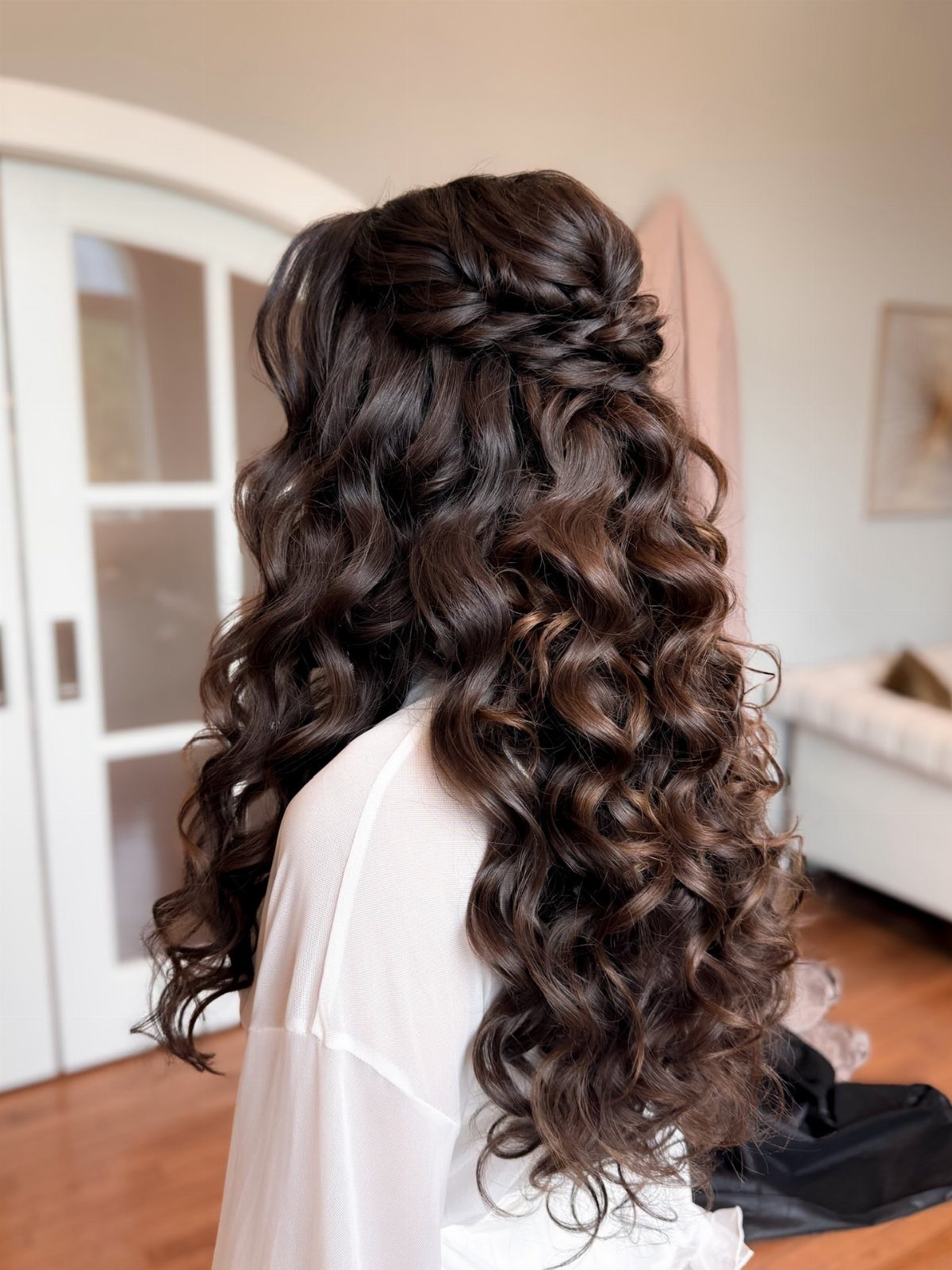 Long dark curls cascade beneath a braided crown on a woman in white