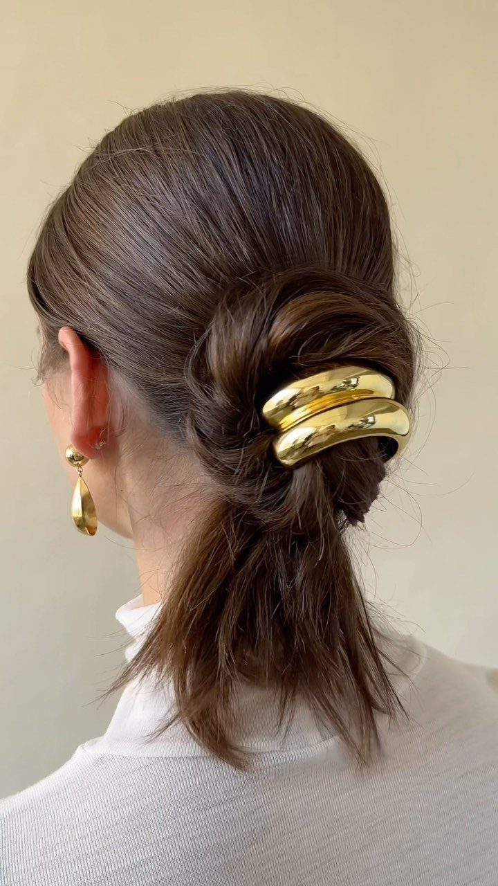 Low dark ponytail secured with a polished gold metallic cuff