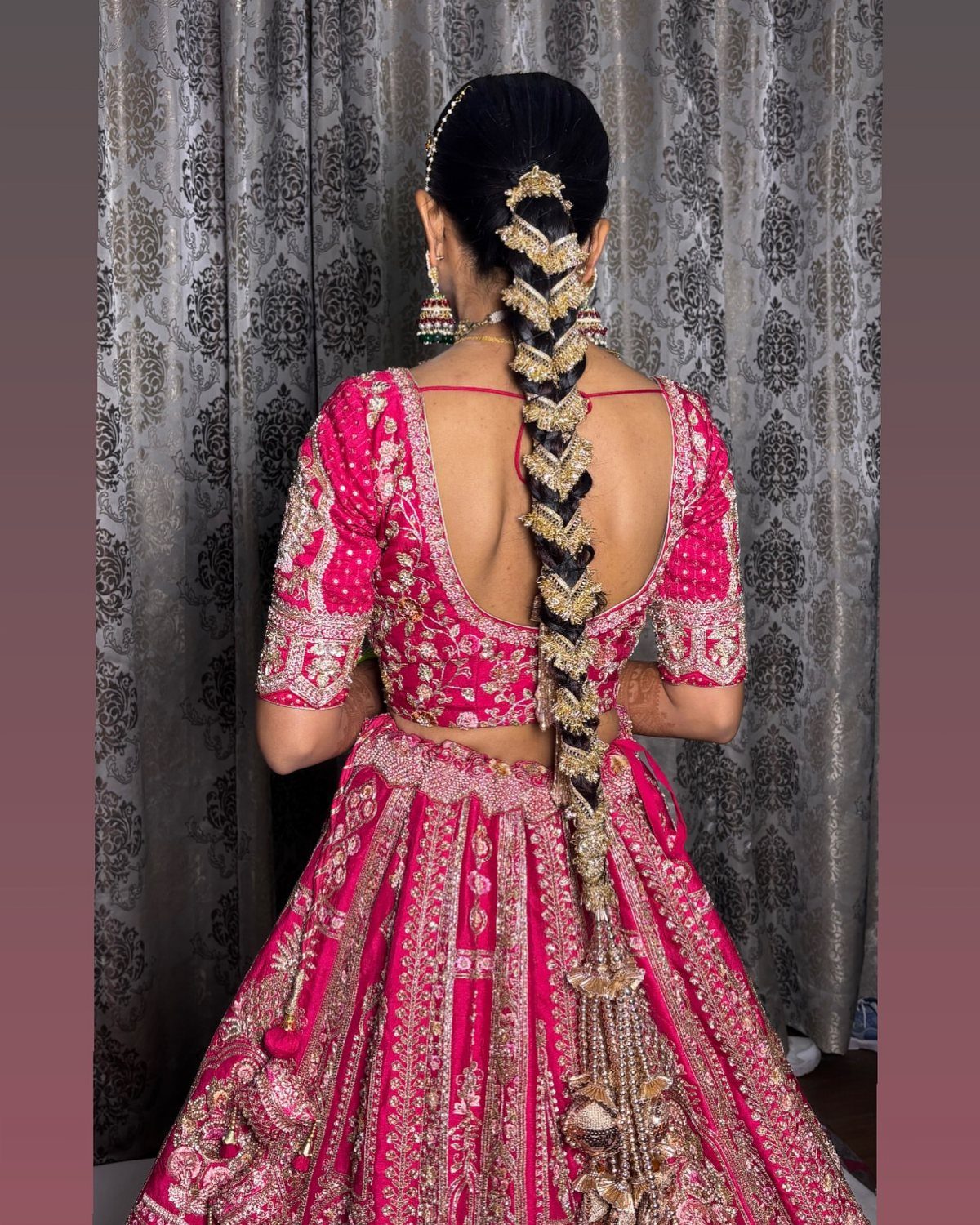 Woman in pink embroidered attire wears a long braid decorated with gold ornaments
