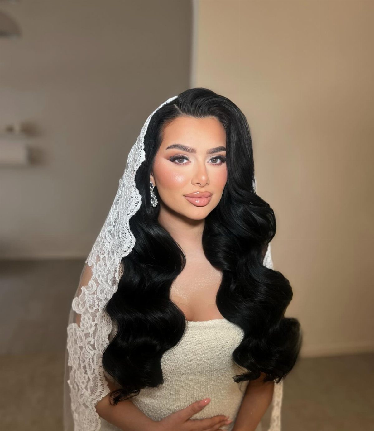 Bride wearing a lace veil with long black hair styled in glossy waves