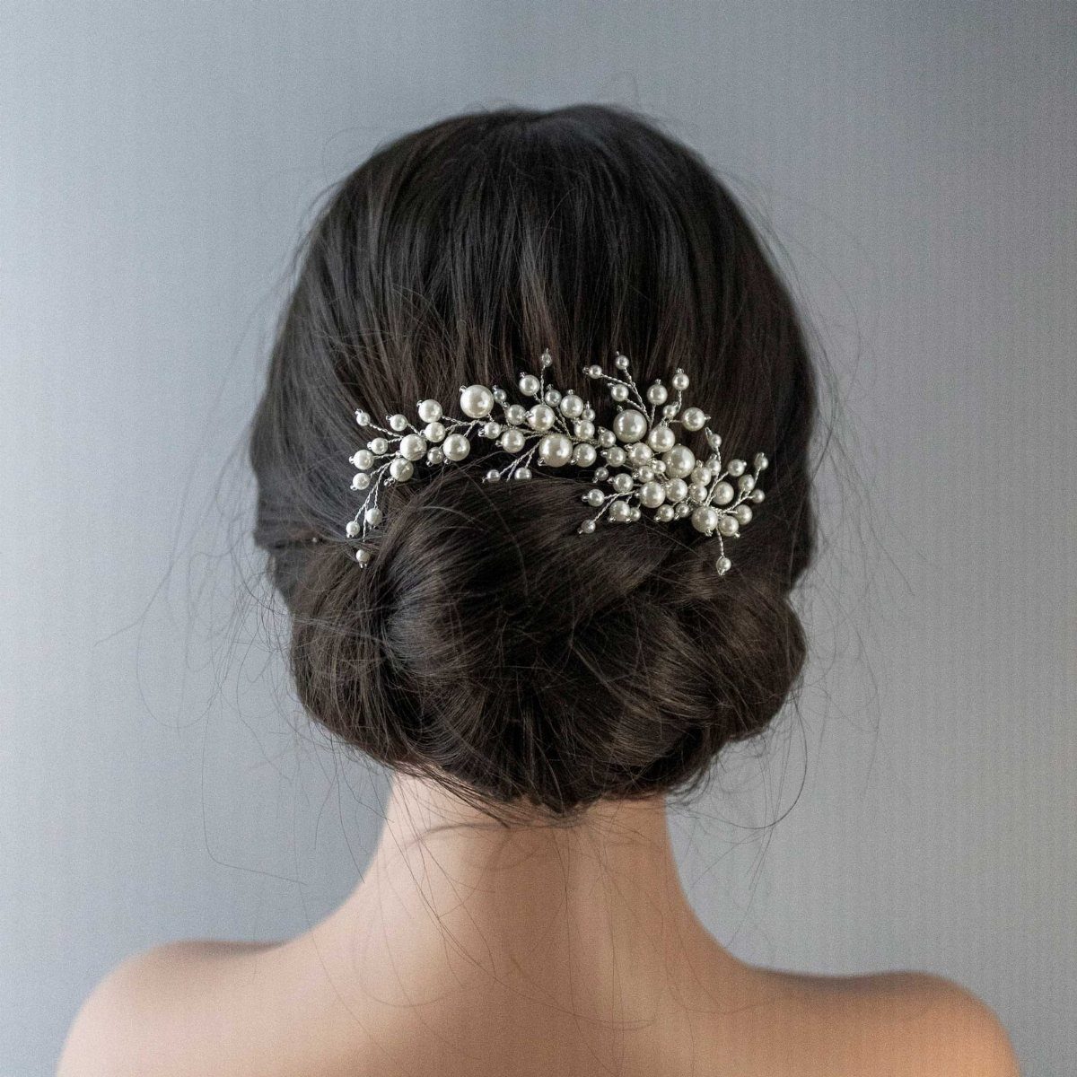 Long dark bridal hair arranged in a low updo with a pearl hairpiece