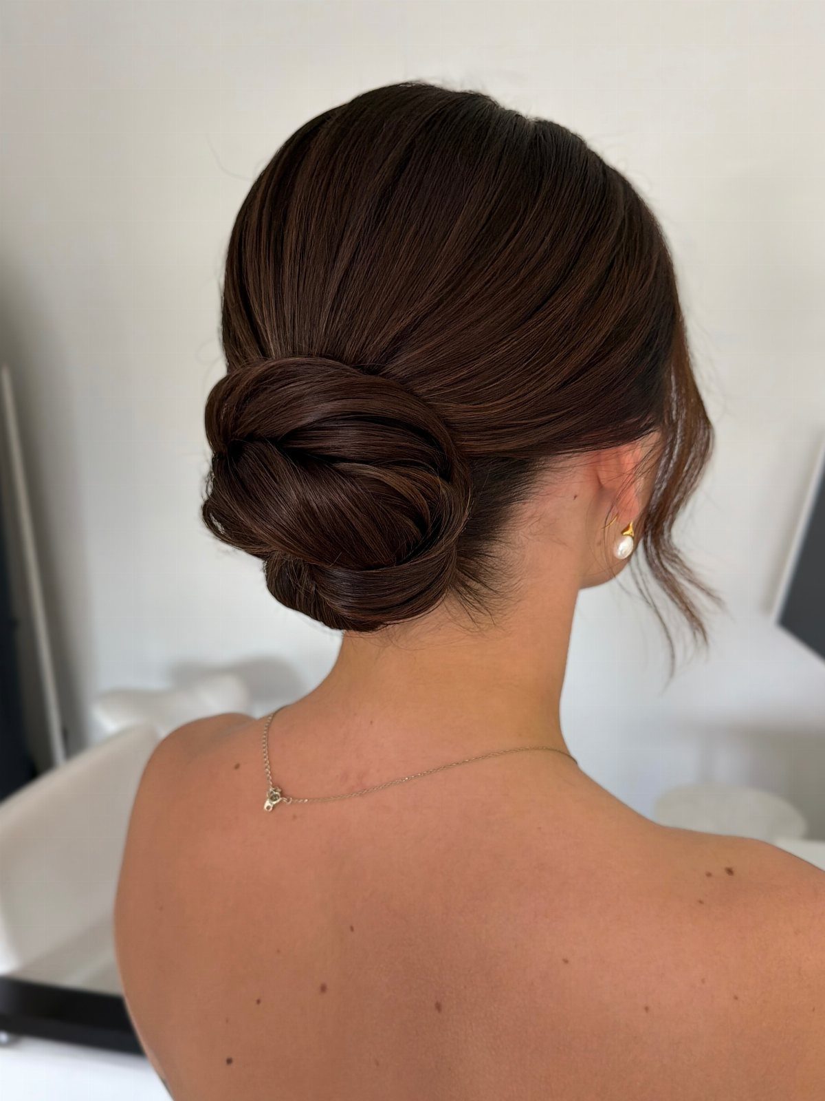 Low chignon pinned neatly at the nape with smooth swept hair