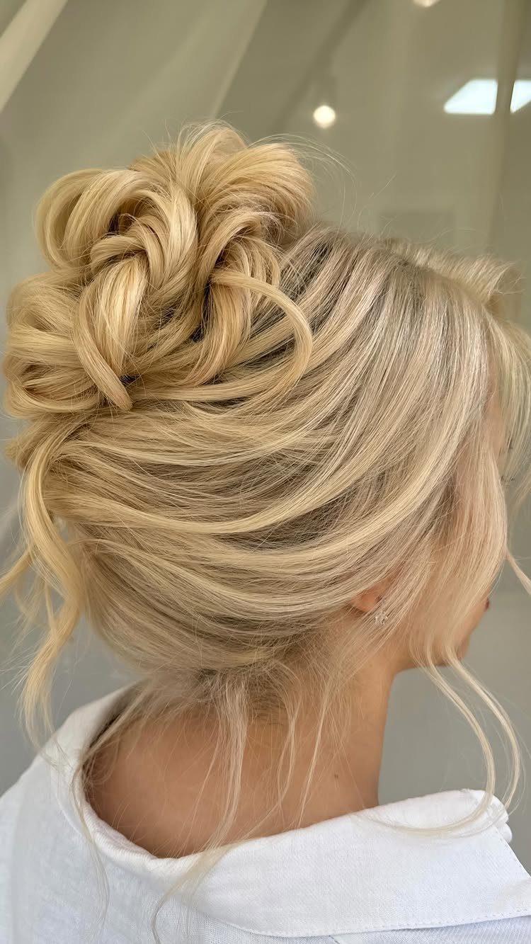 Blonde curled hair twisted into a relaxed, voluminous updo with loose wisps