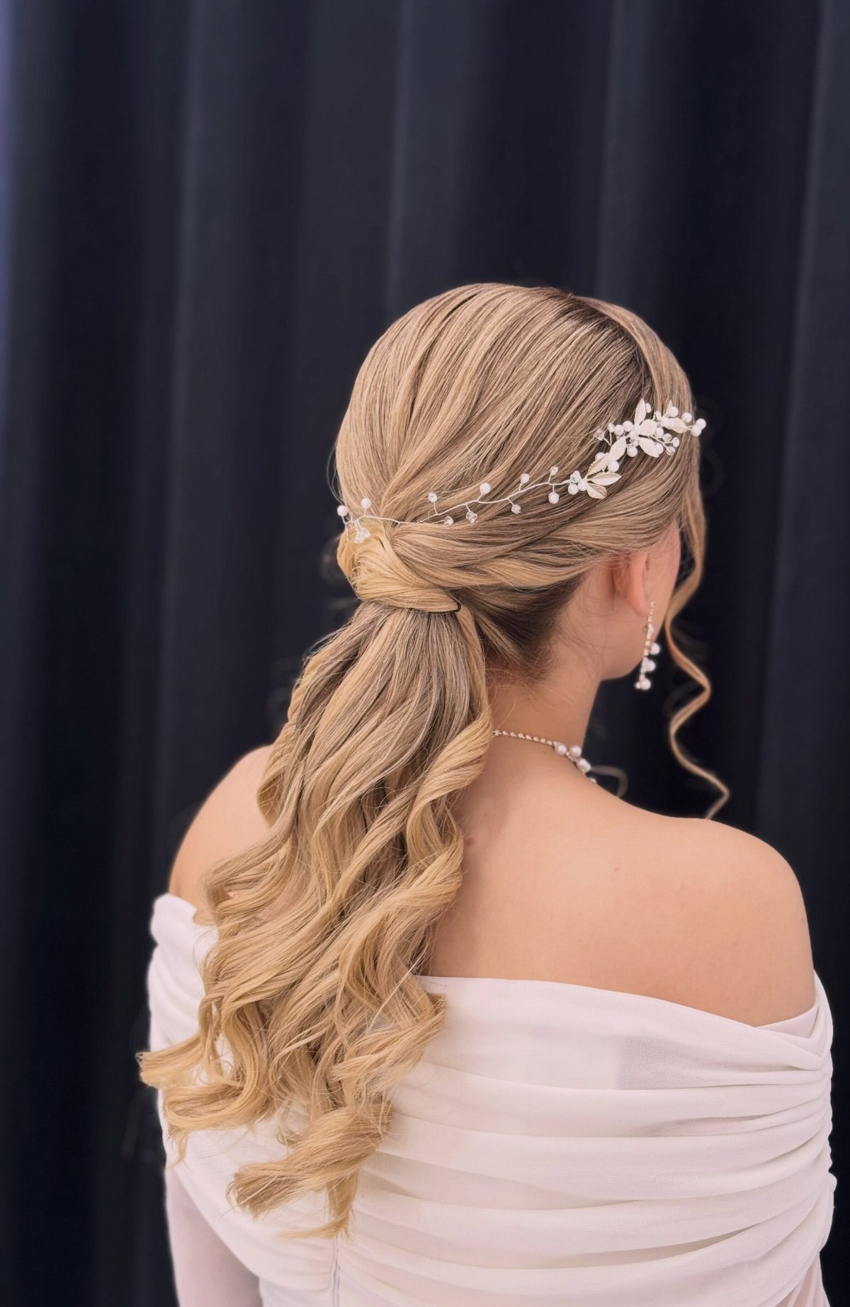 Blonde bride with a curled side-swept ponytail and delicate floral hairpiece