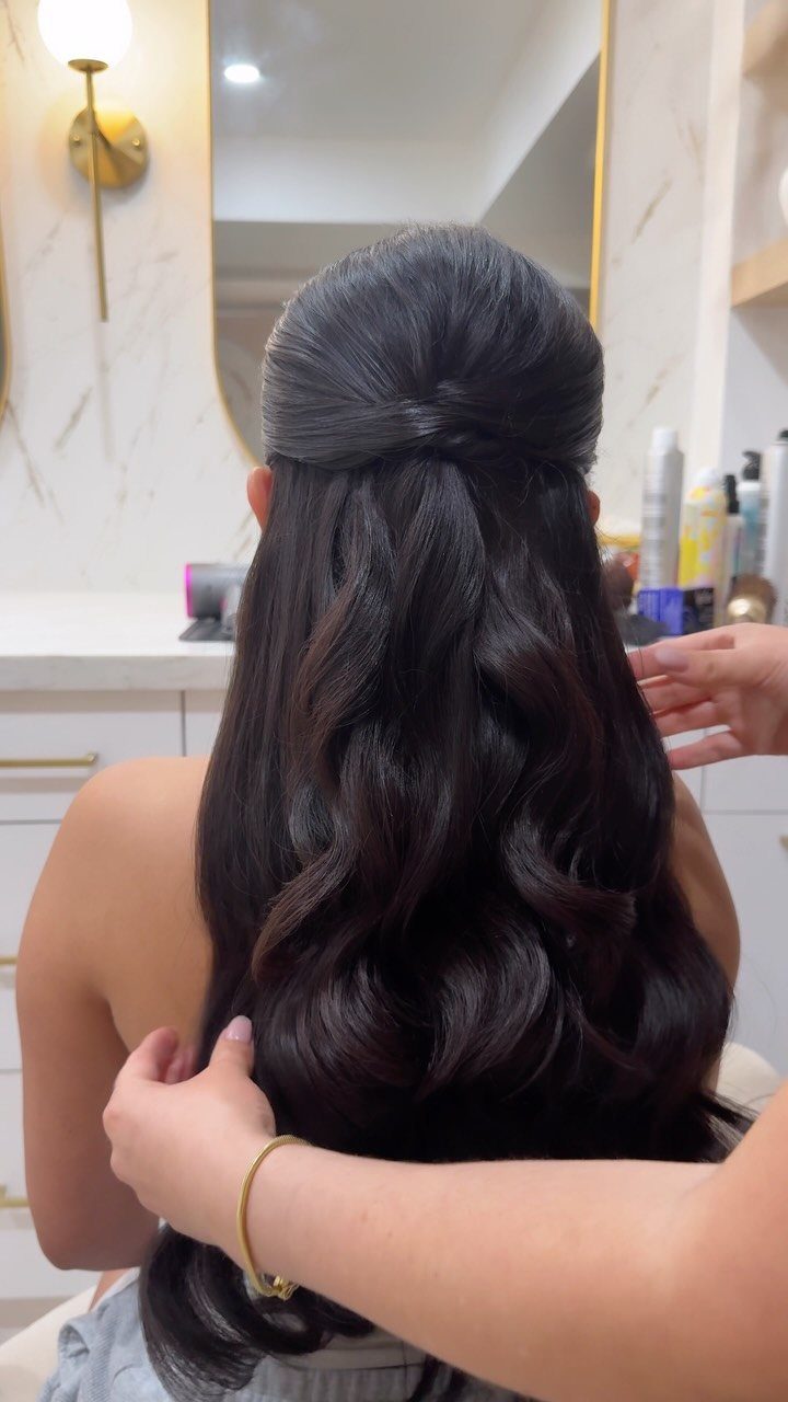 Dark wavy half-up hairstyle being arranged by a stylist from behind