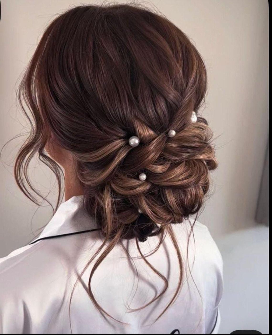 Loose brown bridal bun with pearl pins and curled tendrils