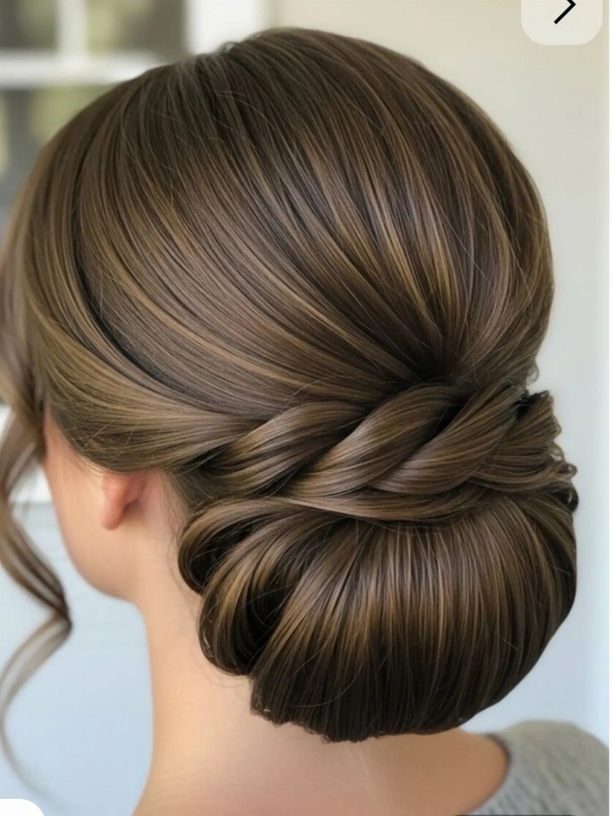 Polished brown low bun with a twisted section wrapped across the nape