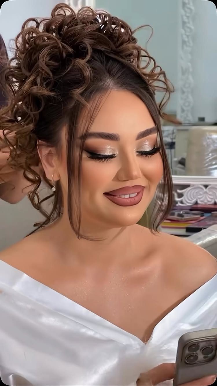 Woman wearing a loose curly updo with tendrils and white satin