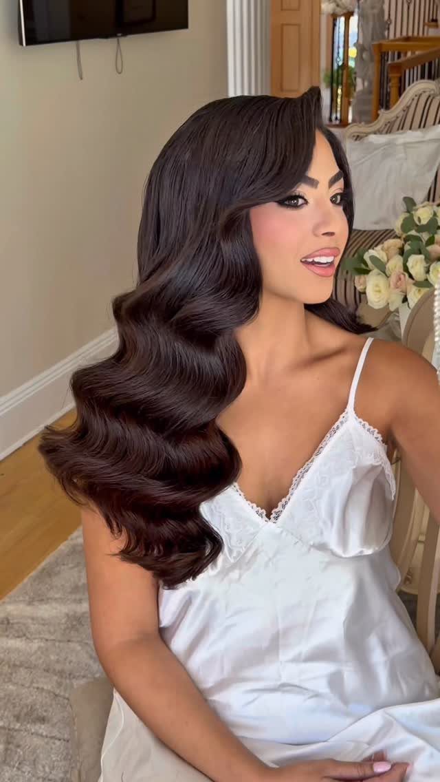 Woman with glossy dark waves swept over one shoulder in a white satin camisole