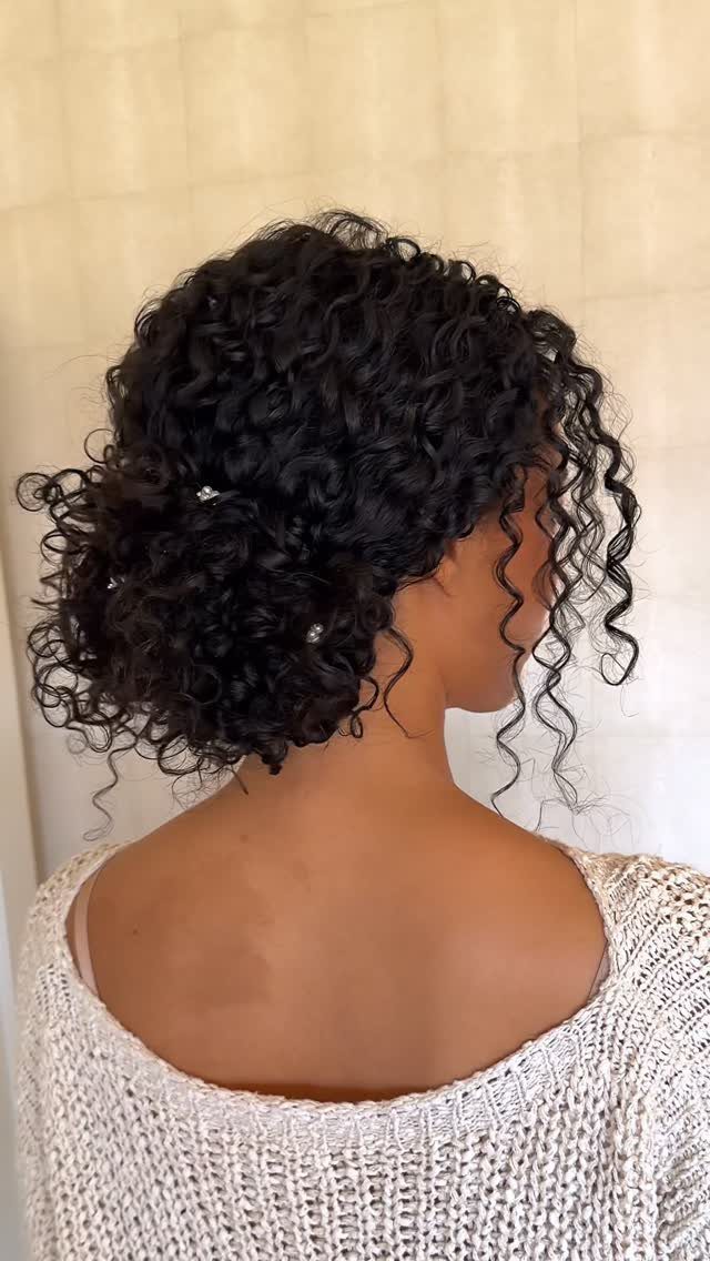 Dark curly updo pinned high, with loose tendrils framing a woman's face