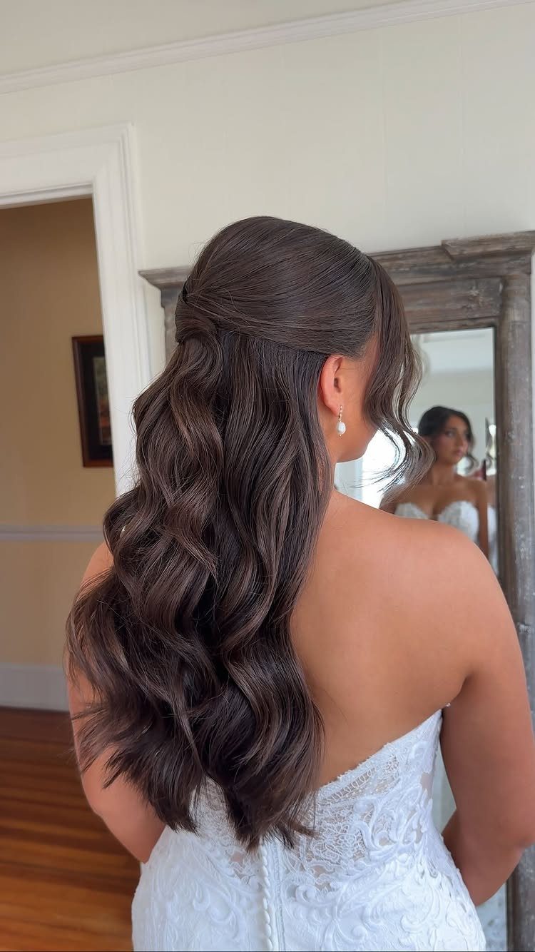 Half-up wavy hairstyle pinned at the crown on a bride in a white lace dress