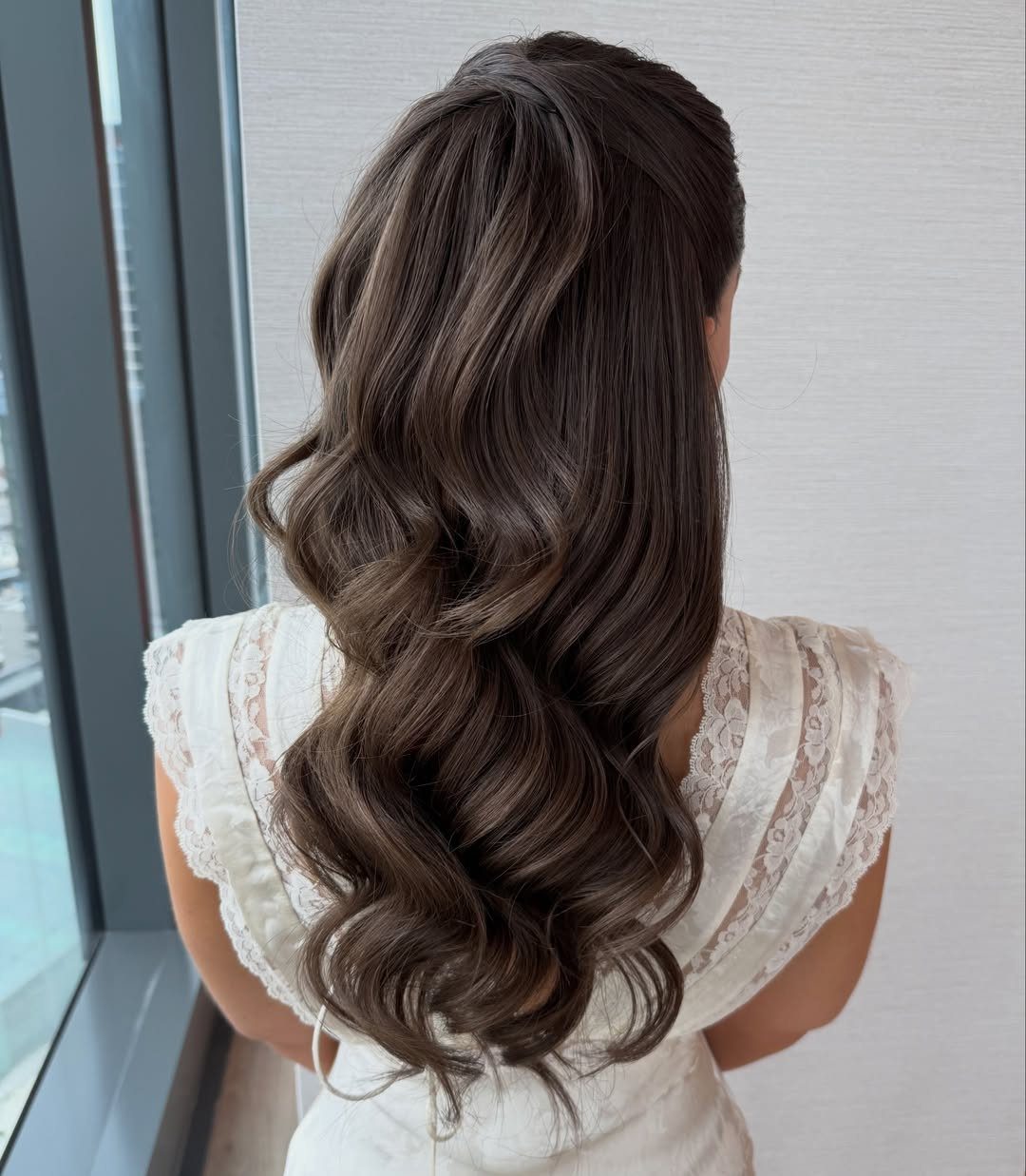 Long dark wavy hair falls down the back of a woman in a lace dress
