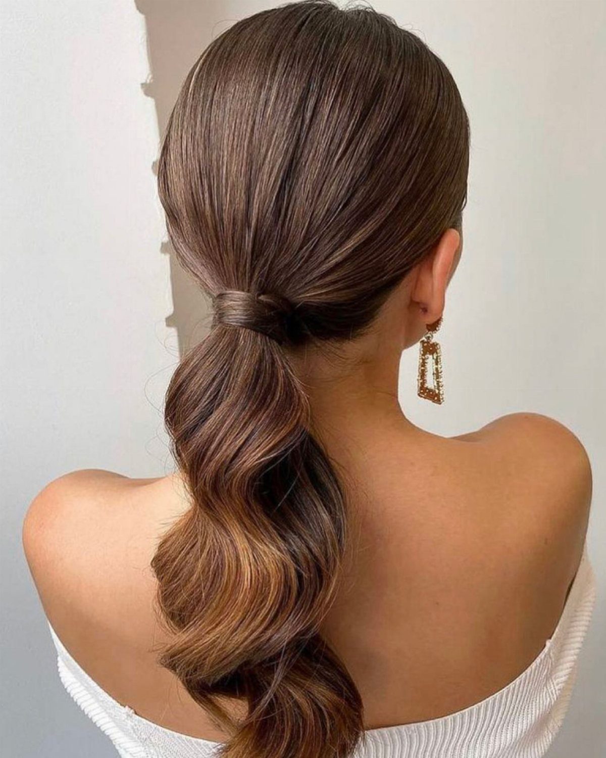 Low wavy ponytail secured with wrapped hair on a woman in a white top