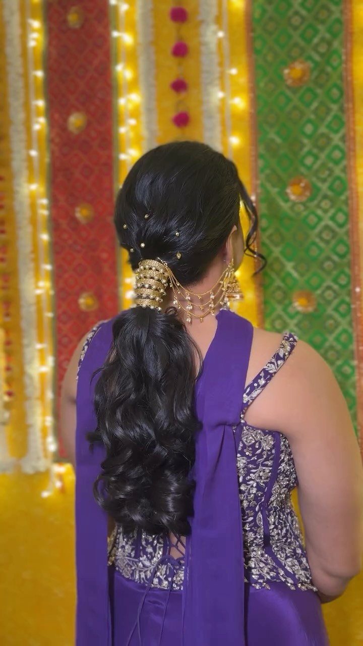 Low wavy ponytail with gold ornament on a woman in purple attire