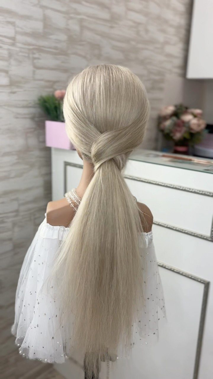Blonde low ponytail with smooth side twists against a pale stone wall