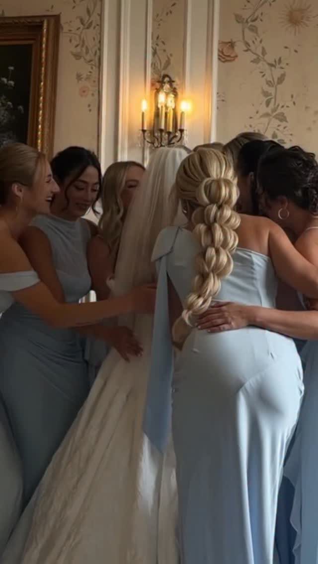 Blonde bride wears a thick segmented pull-through braid among embracing bridesmaids