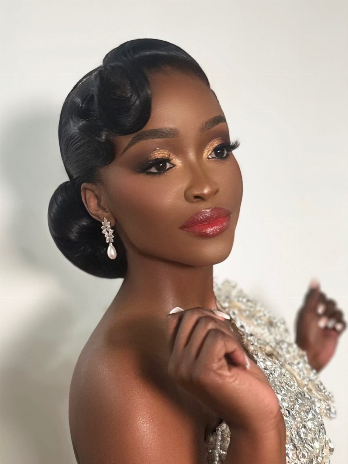 Woman with a sculpted updo and dangling earrings poses in a sparkling white garment
