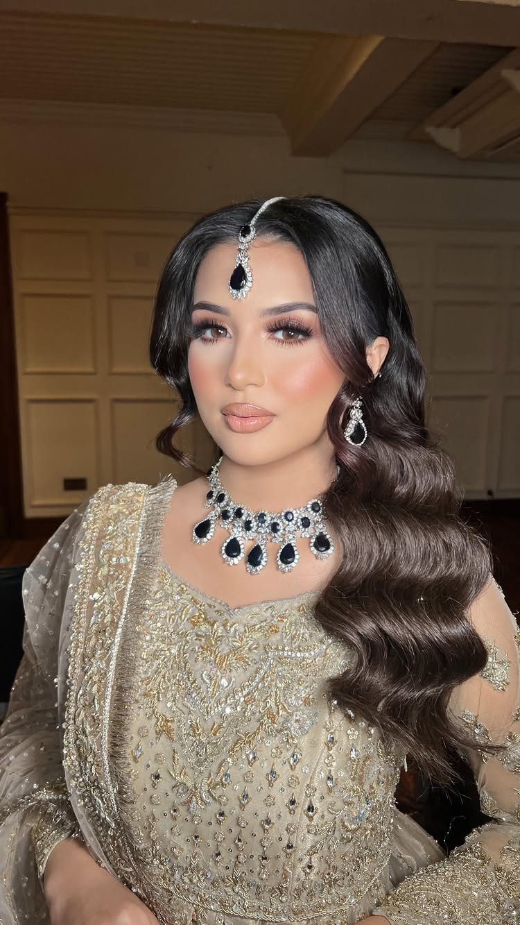 Woman in jeweled attire wearing long dark hair in loose waves over one shoulder