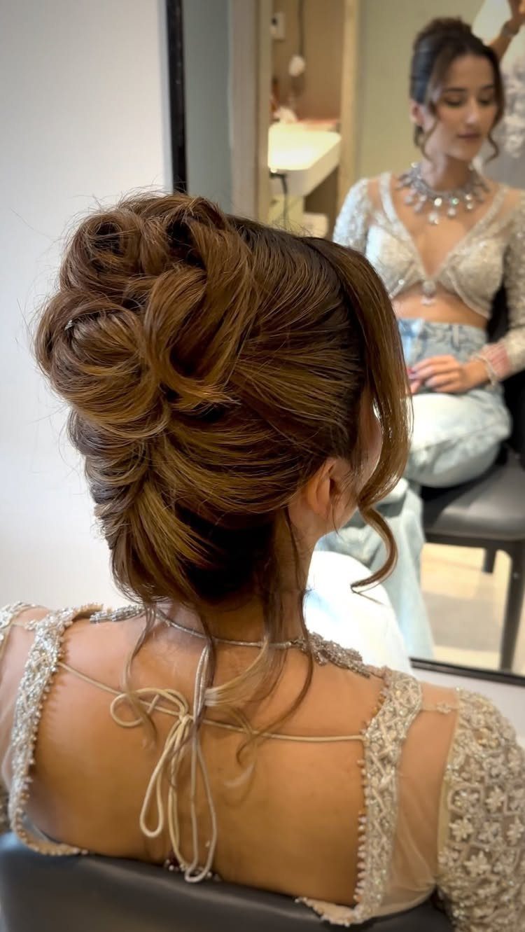 High twisted knot hairstyle shown from behind as a bride faces a mirror
