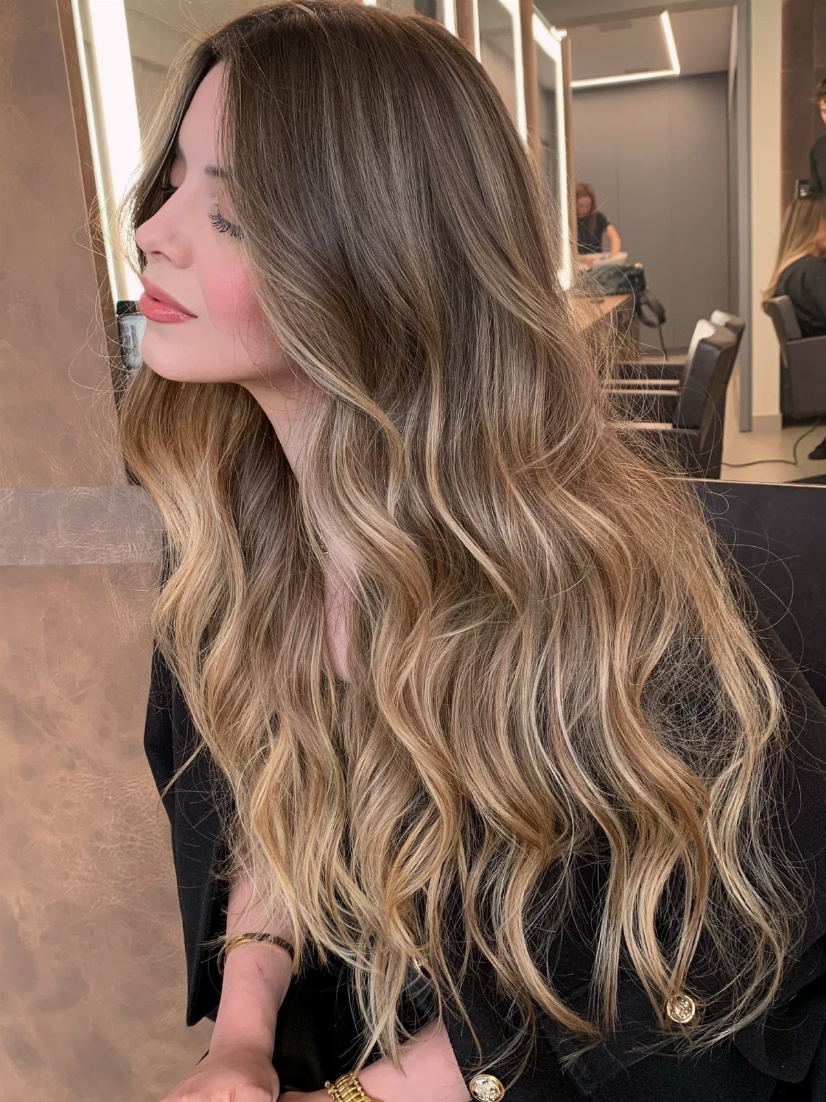 Woman with long wavy brown hair and soft golden balayage