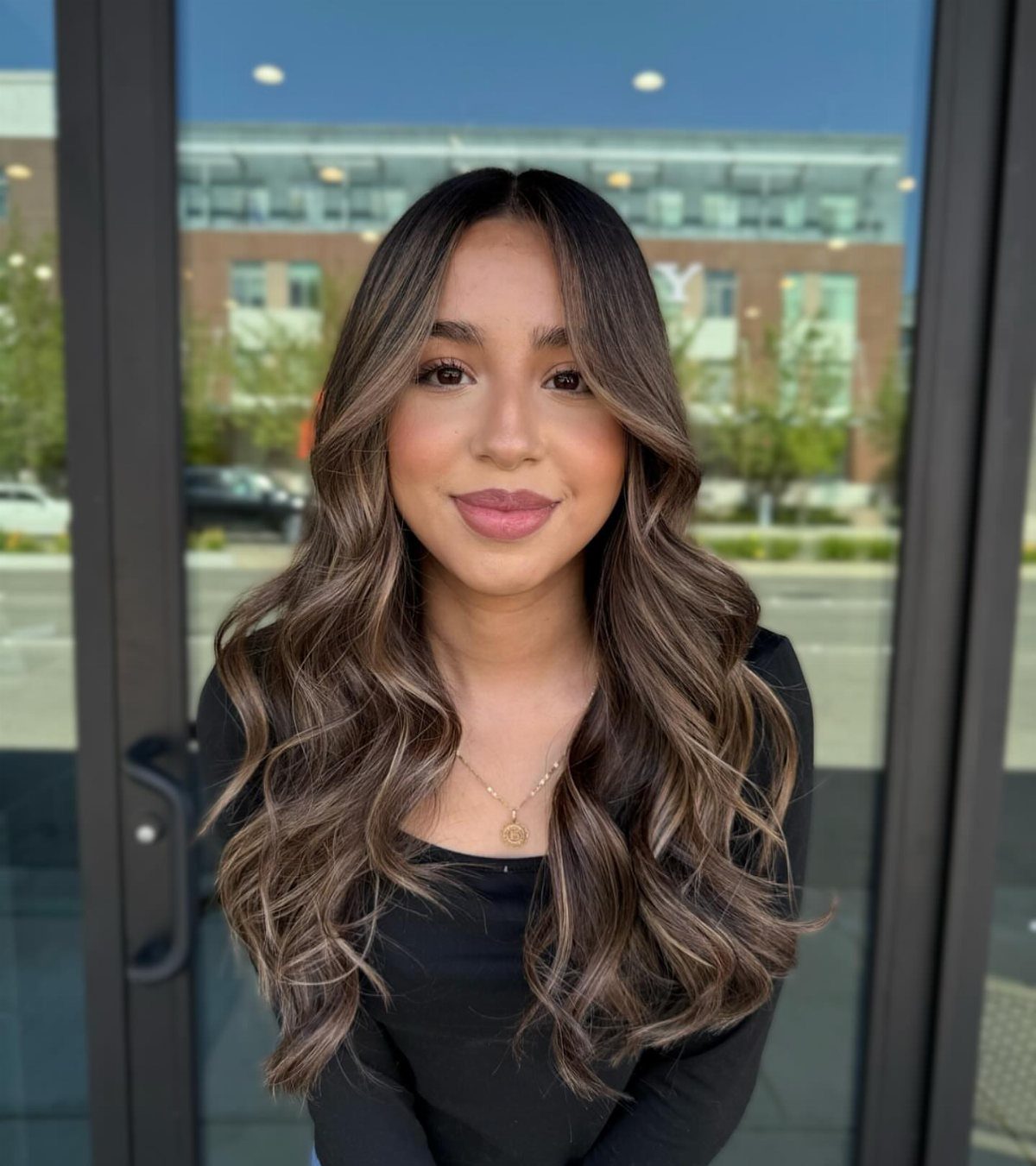 Woman with long wavy brown hair and soft golden balayage highlights